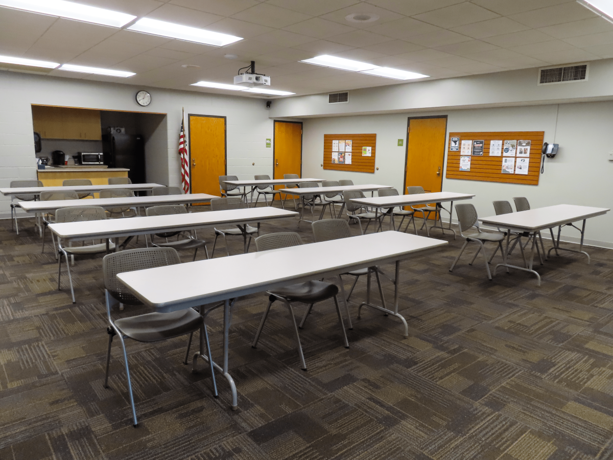 Large Room with 6 rectangular tables with chairs, small kitchenette in back 